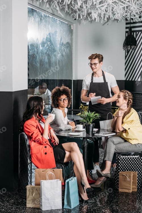 Preview: group of happy young women with shopping bags making order in cafe