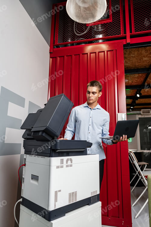 Preview: Positive young man using printer in the modern office