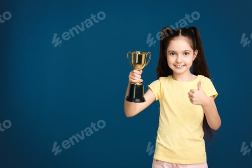 Preview: Happy girl with golden winning cup on dark blue background. Space for text