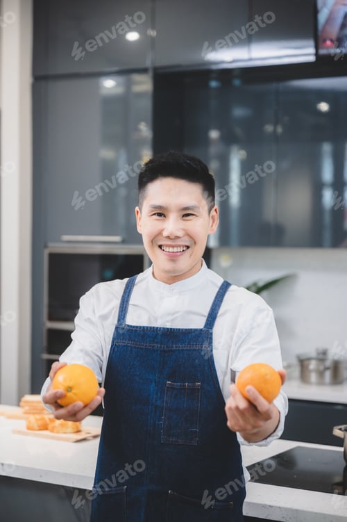 Preview: Smiling and successful male chef wearing apron holding huge lemons in hand while working