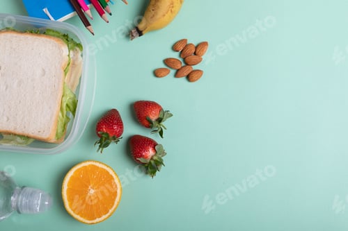 Preview: Overhead view of fruits and sandwiches in tiffin box on green background with copy space