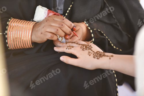 Preview: A younger woman has henna traditionally applied on her skin by an elderly woman at a local festival