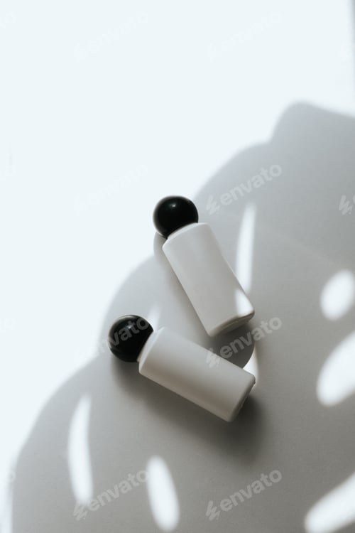 Preview: Two white empty plastic bottles on a white background with a shadow of a tropical leaf