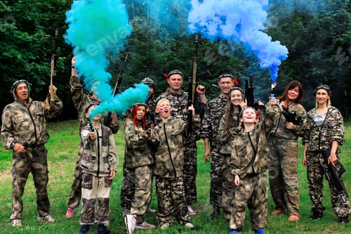 Preview: People in camouflage celebrating winning laser tag shooting game with colored smoke. N