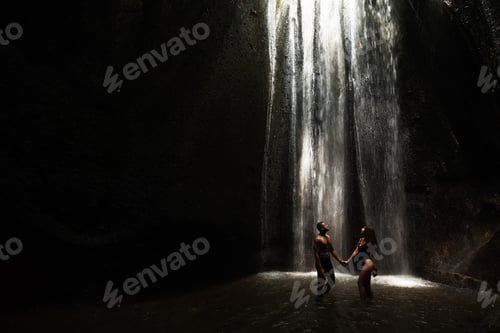 Preview: Beautiful couple in a cave with a waterfall. Athletic man and woman under the streams of a waterfall