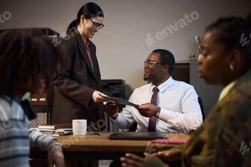 Vista previa: Mujer caucásica de mediana edad que entrega documentos a un hombre negro de mediana edad que trabaja