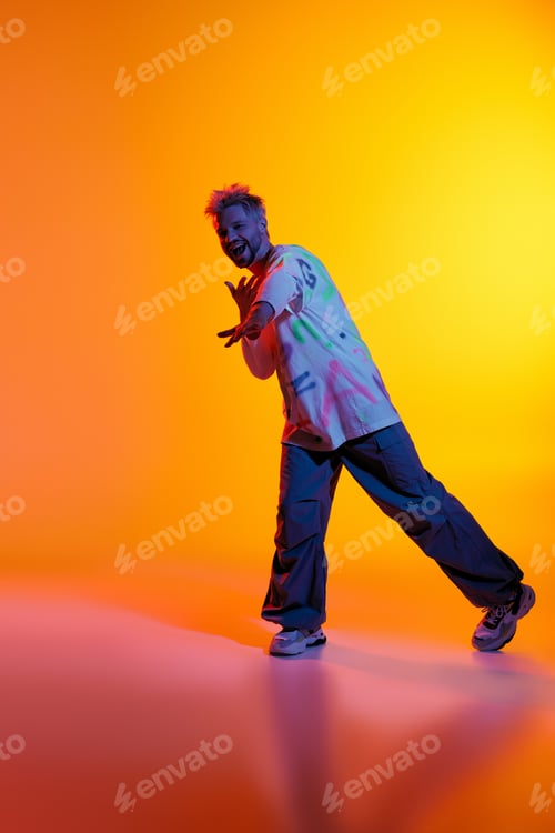 Preview: Striking poses under vibrant lighting by a handsome young man in casual attire
