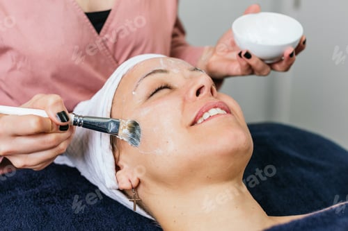 Preview: Anonymous professional beautician applying facial mask on face of client