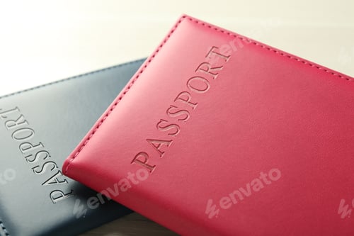 Preview: Two passports in bright covers on white wooden table, closeup