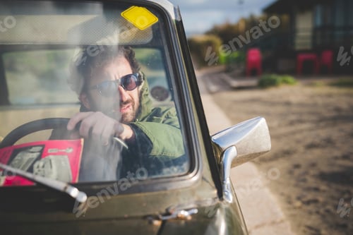 Preview: Man in parked vintage car looking through wing mirror