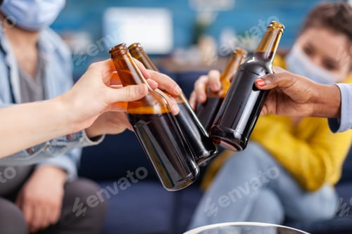 Preview: Happy diverse young people having fun in living room, clinking bottles