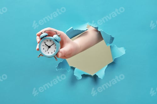 Preview: Hand holds alarm clock through a paper hole. Time management and deadline concept