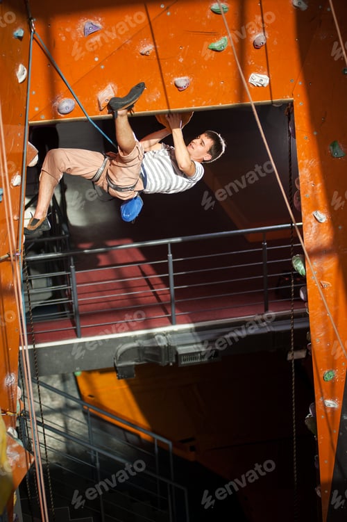 Preview: Male rock-climber practicing climbing on rock wall indoors