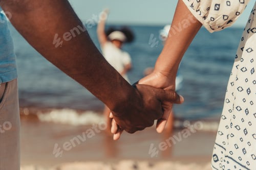 Preview: close-up partial view of african american couple holding hands while standing at seaside