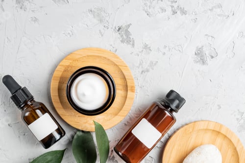 Preview: Moisturizer cream jar, serum in glass bottle and green leaves on concrete background. Flat lay, top