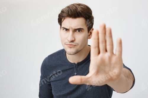 Preview: Serious confident angry european man with stubble wearing casual clothes posing against gray studio