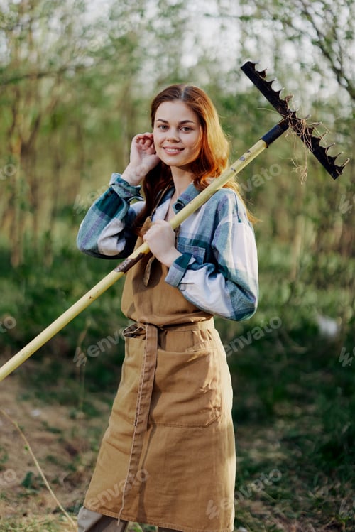Preview: Woman beautifully smiling farmer in work clothes and apron working outdoors in nature and holding a