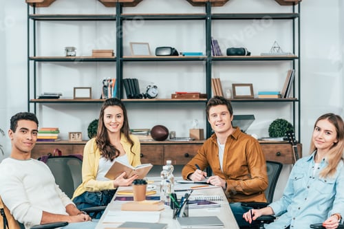Preview: Four multicultural smiling students sitting at table and looking at camera