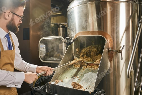 Preview: Brewery worker holding shovel with milled malt grains