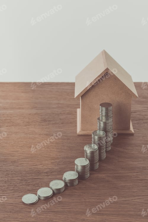 Preview: stacks of coins and small wooden house on wooden table, saving concept