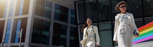 Preview: Two woman in trendy outfits walk outside on background of modern building