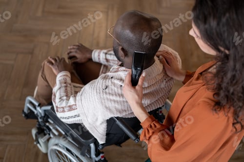 Preview: Above angle of black man with disability having his hair cut by caregiver