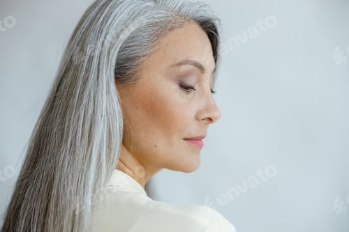 Preview: Pretty middle aged Asian woman with loose straight grey hair on light background