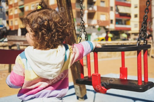 Preview: Backview of a toddler girl with beautiful curly brunette hair wearing a rainbow hoody