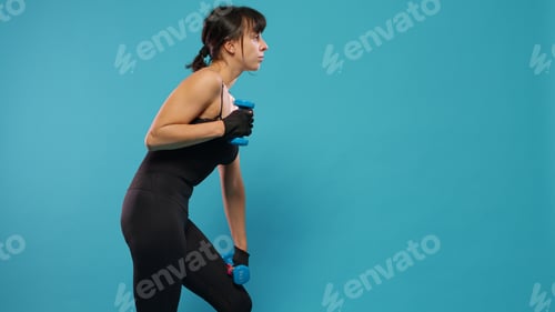 Preview: Athletic woman using dumbbells to do workout exercise in studio