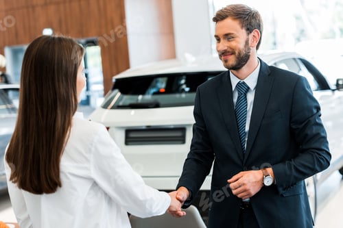 Preview: happy car dealer shaking hands with woman in car showroom