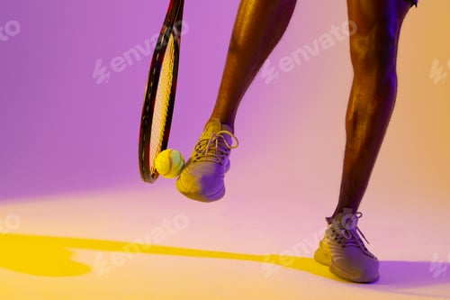 Preview: Image of legs of african american male tennis player in violet and yellow neon lighting