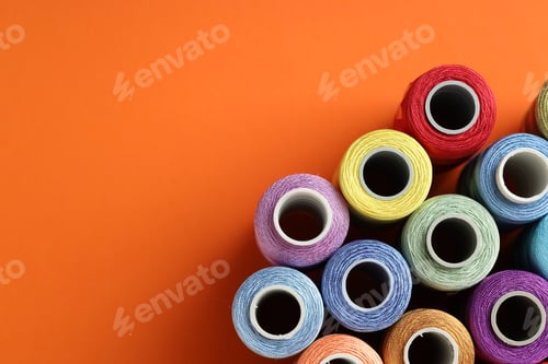 Preview: Different spools of sewing threads on orange background, flat lay. Space for text