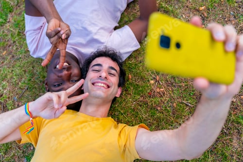 Preview: Couple of multiethnic men in a park, lgbt concept, lying on the grass taking a selfie with a mobile