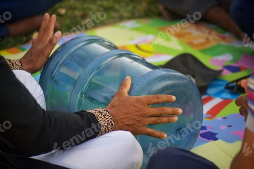 Preview: Diverse brown skinned unrecognizable male musician plays an improvised plastic water bottle drum