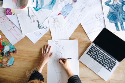 Preview: top view of young fashion designer sketching at workplace