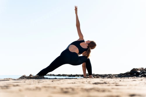 Preview: Woman practicing revolved triangle pose on sandy beach at sunrise
