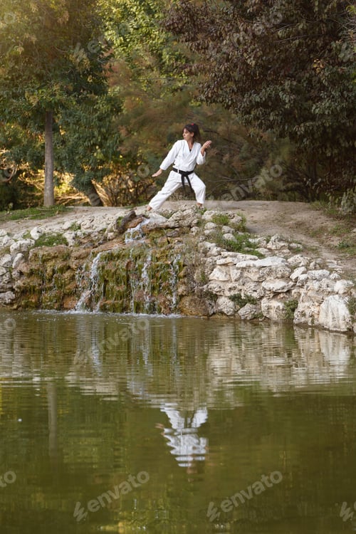 Preview: Sporty woman in kimono and black belt training karate in the nature.