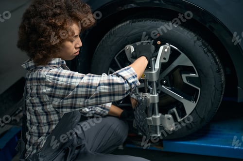 Preview: Young woman adjusts wheel alignment in auto repair shop