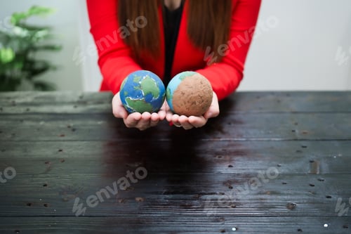 Preview: A young, smiling businesswoman holds a globe her desk, symbolizing global environmental awareness