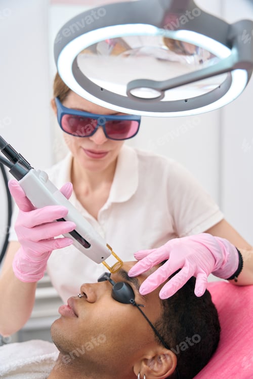 Preview: Beautician removing unwanted hair in glabellar area of young man