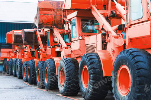 Preview: Row of orange heavy-duty dump trucks parked in industrial area.