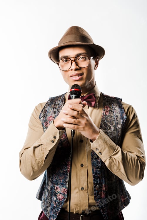 Preview: stylish mixed race man in hat and eyeglasses singing in microphone isolated on white