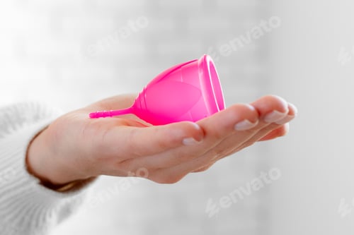 Preview: Woman in white sweater holding pink menstrual cup in hands close up