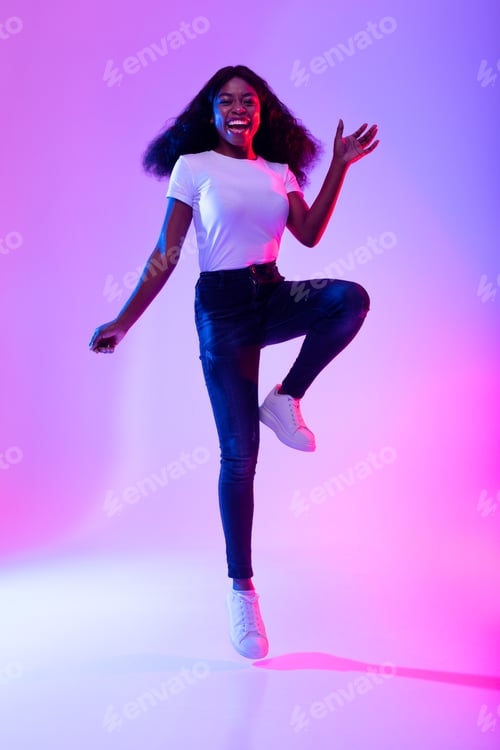 Preview: Full length portrait of active energetic young black woman jumping in neon light