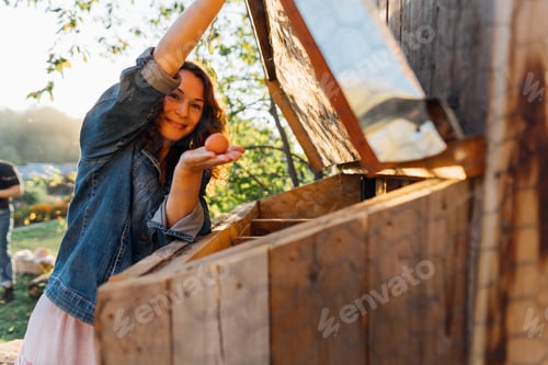 Preview: Outdoor enthusiast in denim smiles upon finding an egg in the chicken nest