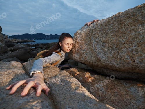 Preview: A determined young woman struggling against large rocks by the sea, showcasing emotions of