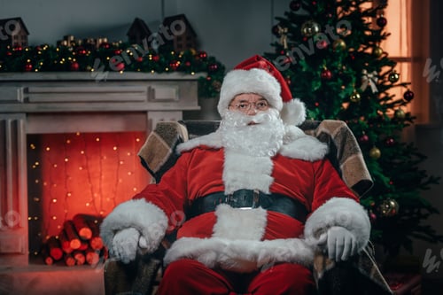 Preview: bearded santa claus in traditional red costume sitting in armchair near fireplace
