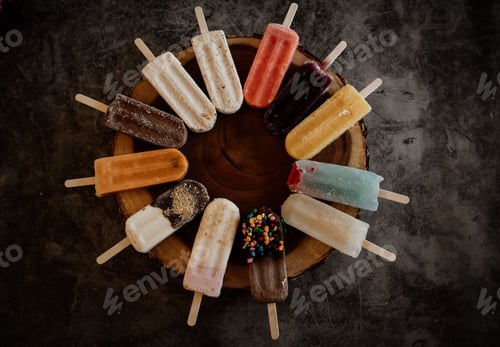 Preview: Top view of a variety of colorful popsicles arranged in a circle on a wooden surface