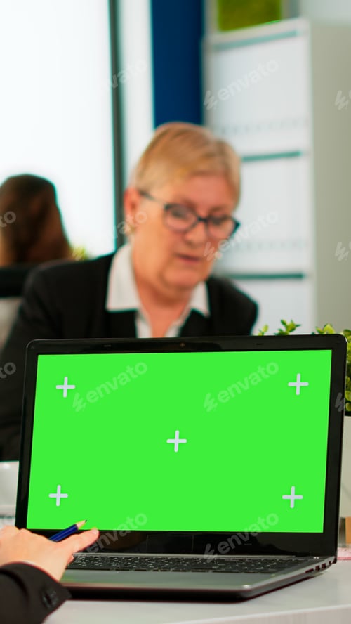 Preview: Over the sholder of manager sitting at meeting desk looking at laptop with green screen