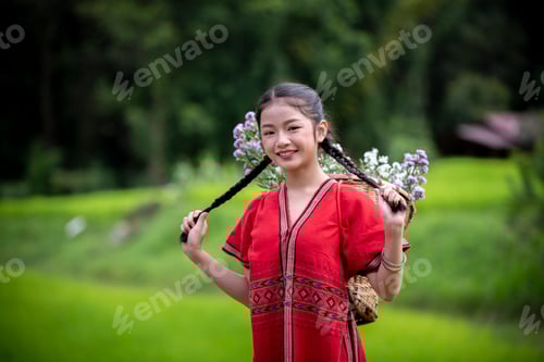 Preview: young girl dressed in traditional clothing, carrying a basket filled with flowers on her back. She i